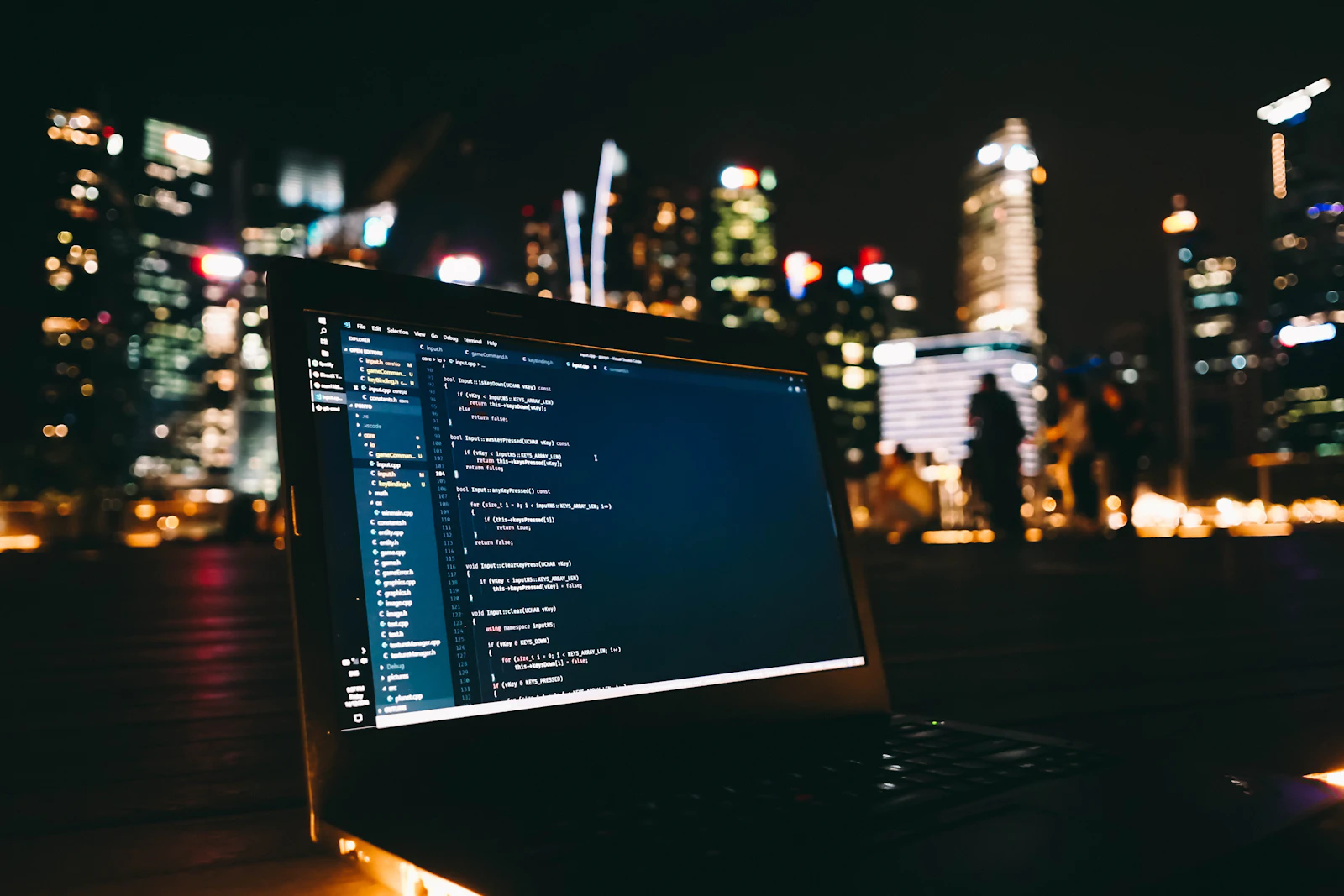 Laptop con código en pantalla y luces de la ciudad al fondo, desarrollo de software para colegios